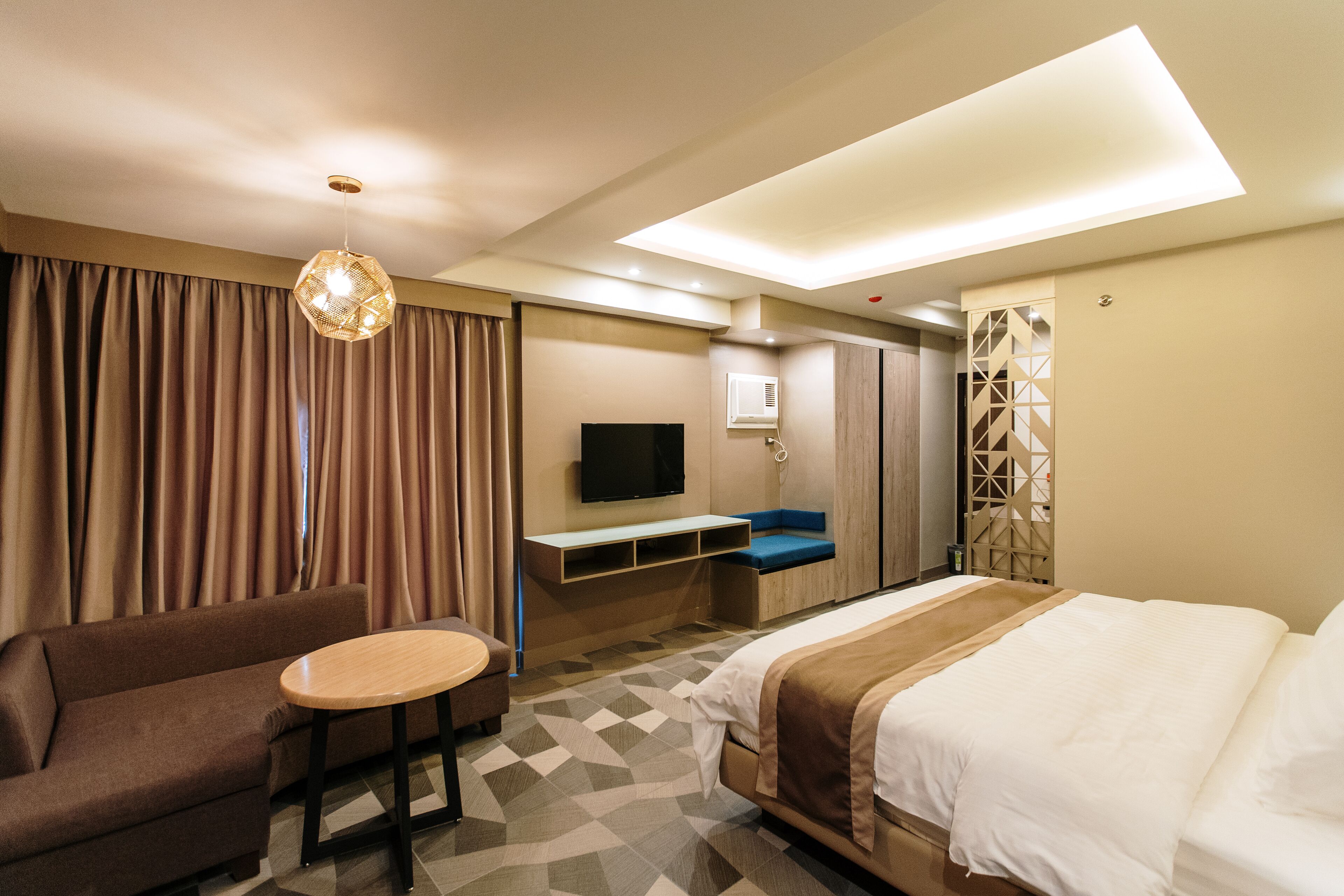 A hotel room with a bed, a sofa, a small table, a TV, and a desk.