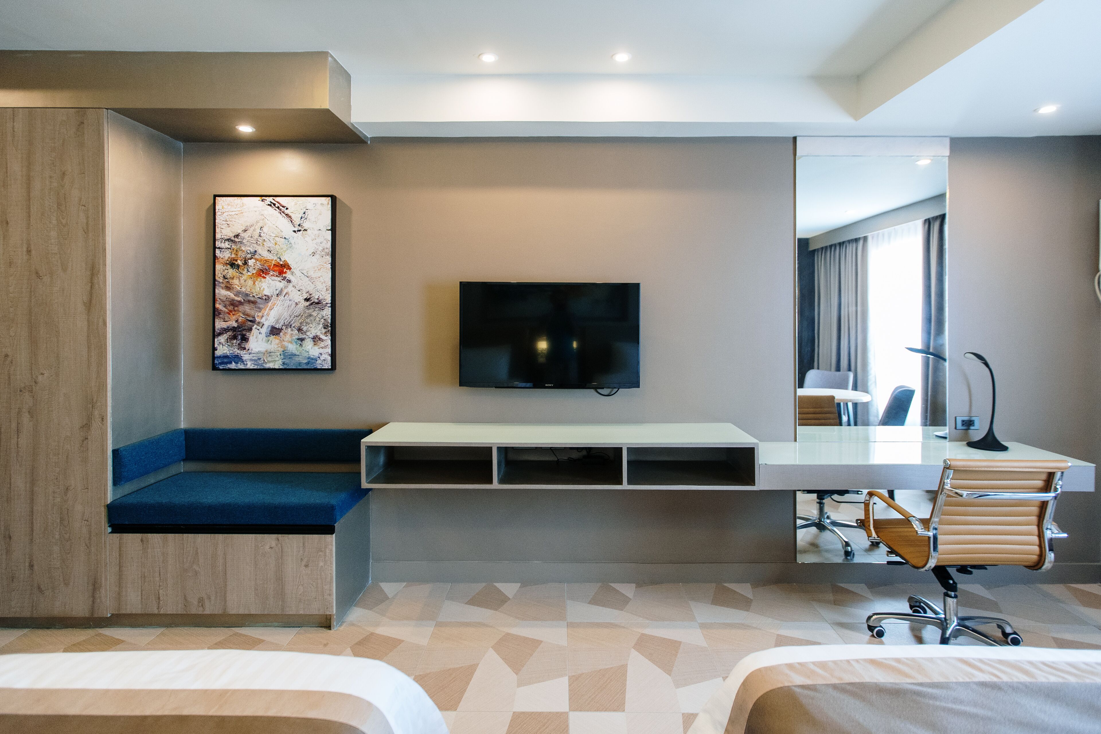 A modern hotel room with a large bed, a desk with a chair, a television, and a painting on the wall.