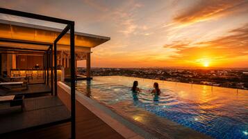 An infinity pool with a sunset view, a bar area, and lounge chairs.