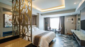 A hotel room with a large bed, a desk, a chair, and a TV.