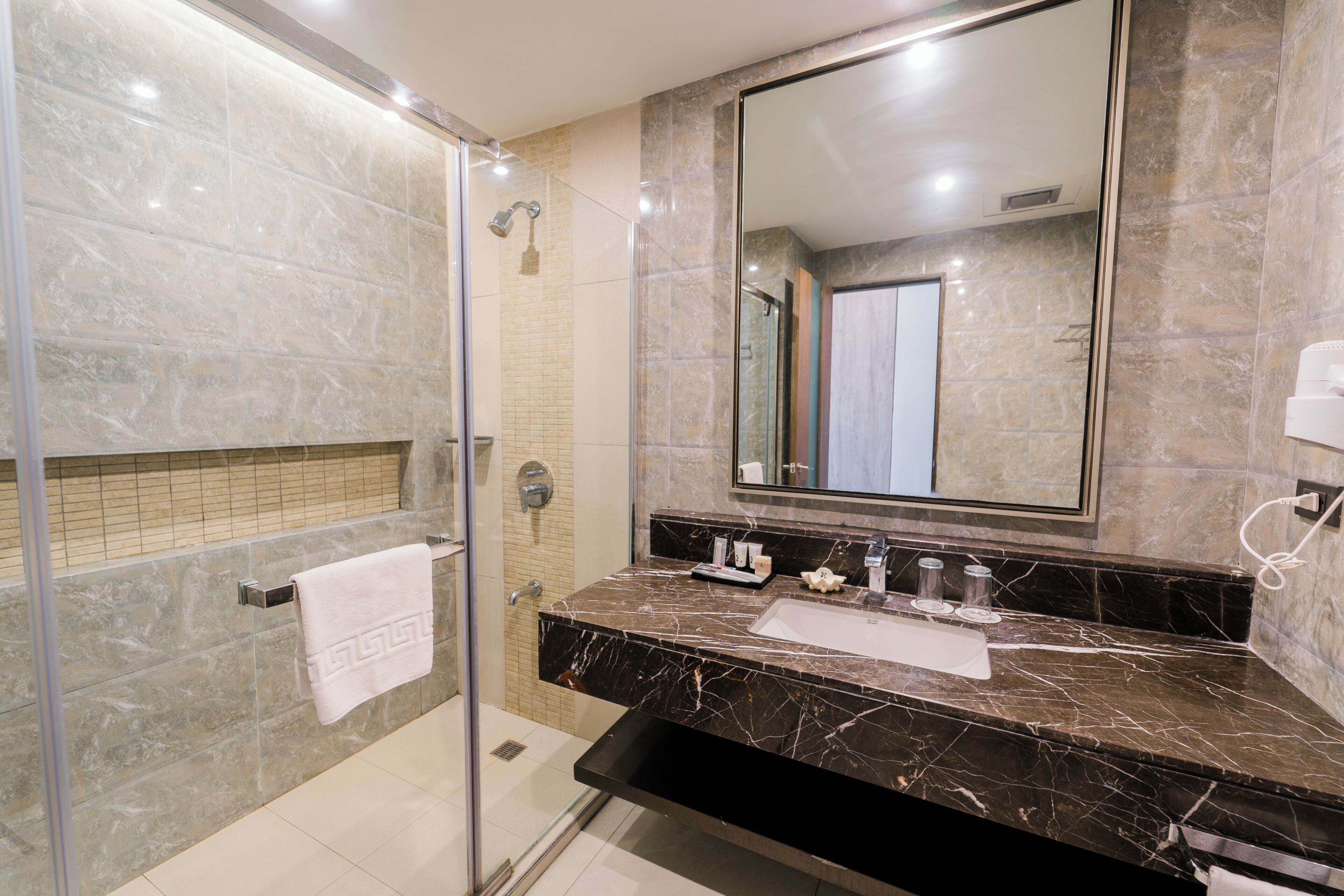 Un baño moderno con ducha de vidrio, lavamanos de mármol y un espejo grande.