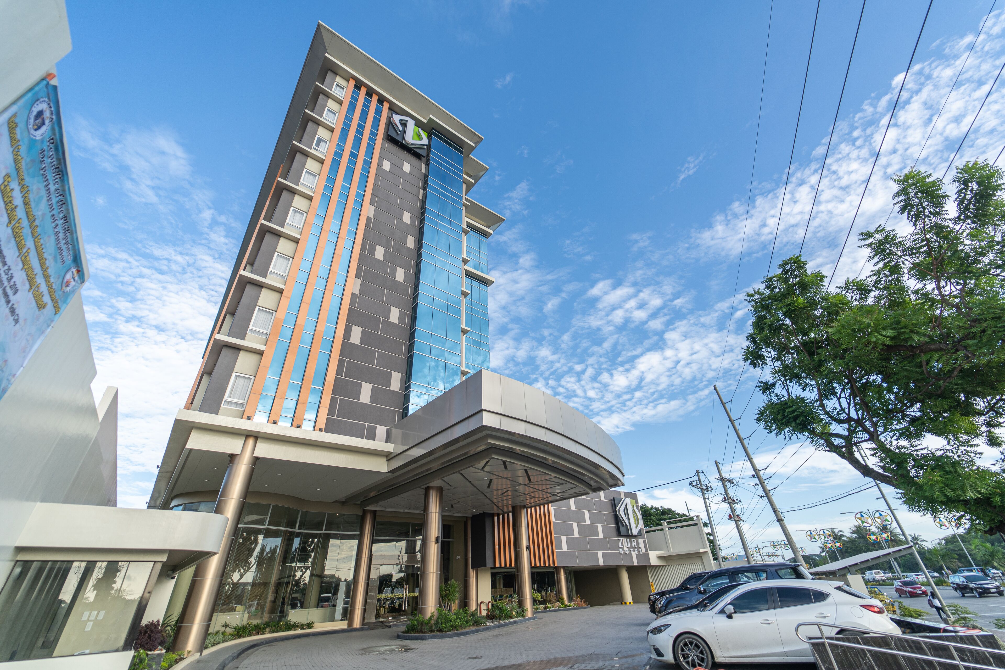 A modern hotel with a curved entrance, multiple floors, and a prominent logo on the facade.