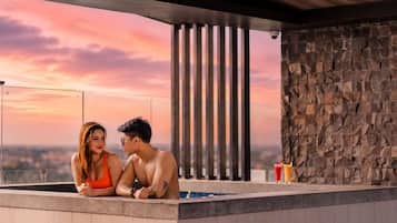 A couple in a hot tub with a sunset view, stone wall, and vertical columns.