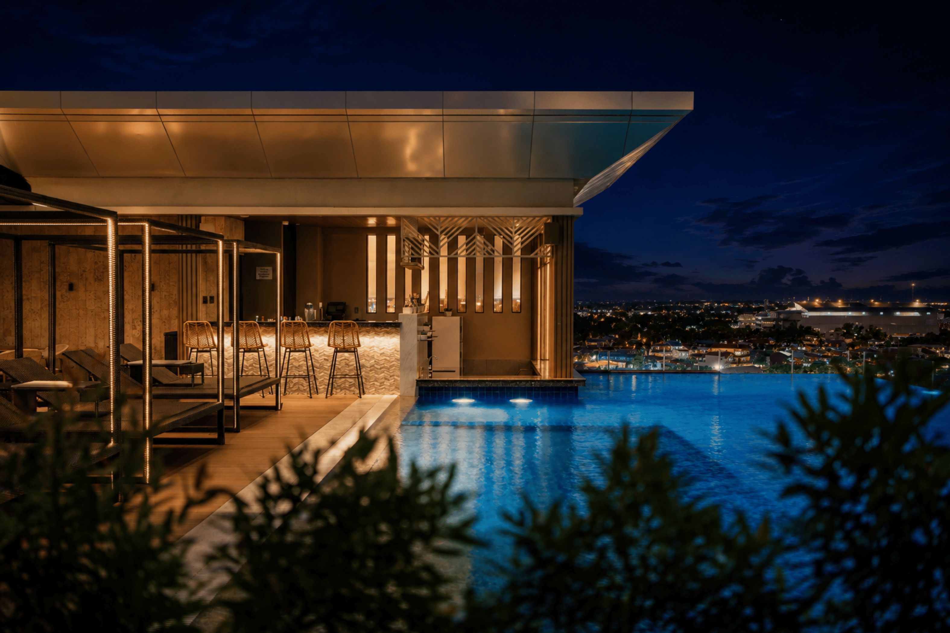 Un bâtiment moderne doté d’une piscine, d’un espace extérieur aménagé et offrant une vue sur la ville la nuit.