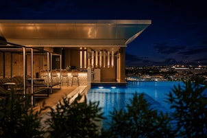 A modern building with a pool, outdoor seating, and a view of the city at night.