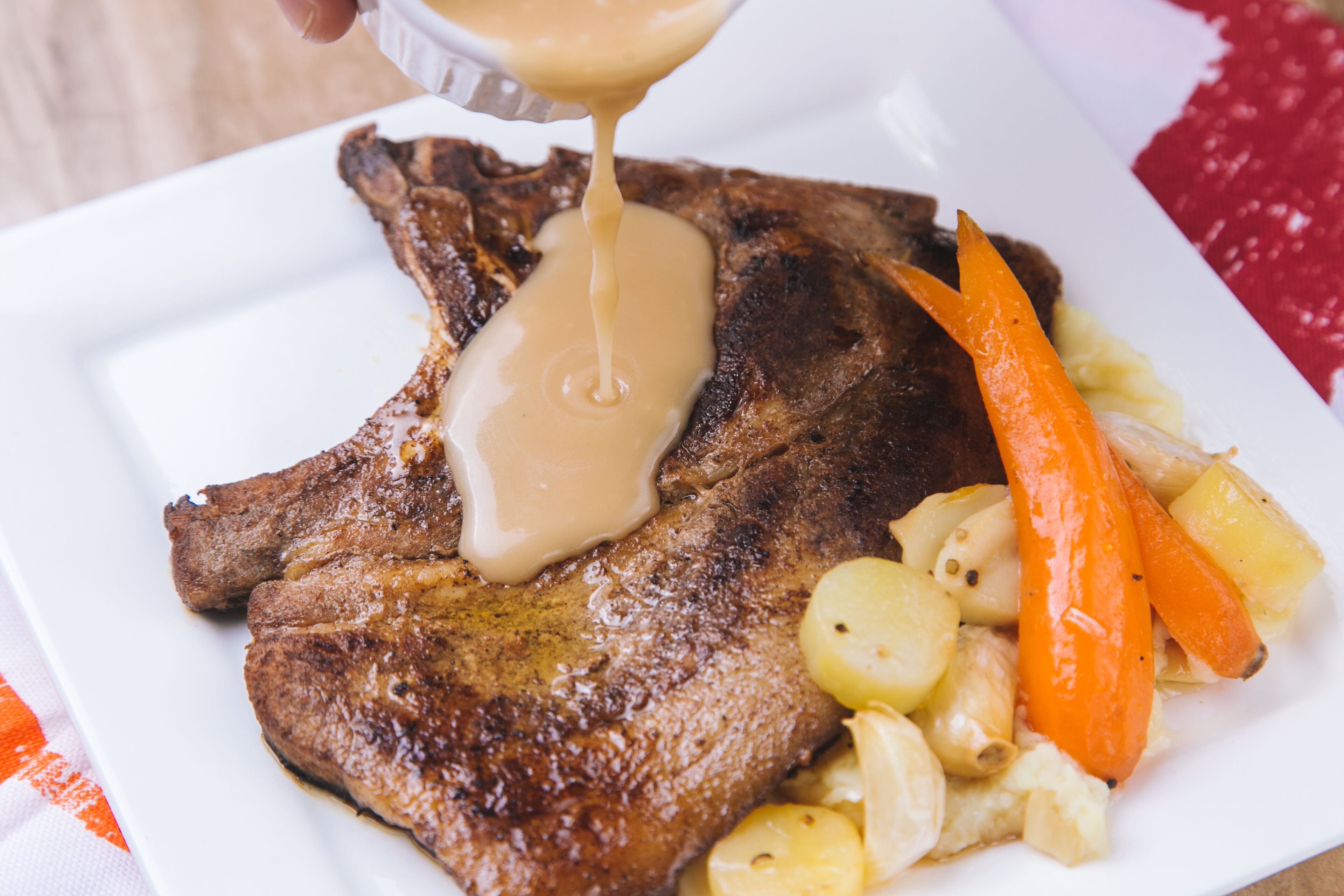 A steak with gravy and vegetables on a white plate.