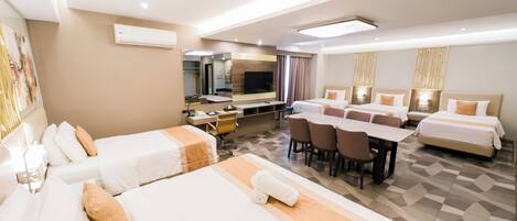 A hotel room with two beds, a desk, a chair, a TV, and a dining area.