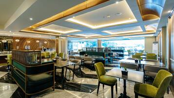 A modern hotel lobby with a reception desk, seating areas, and large windows offering views of the outdoors.