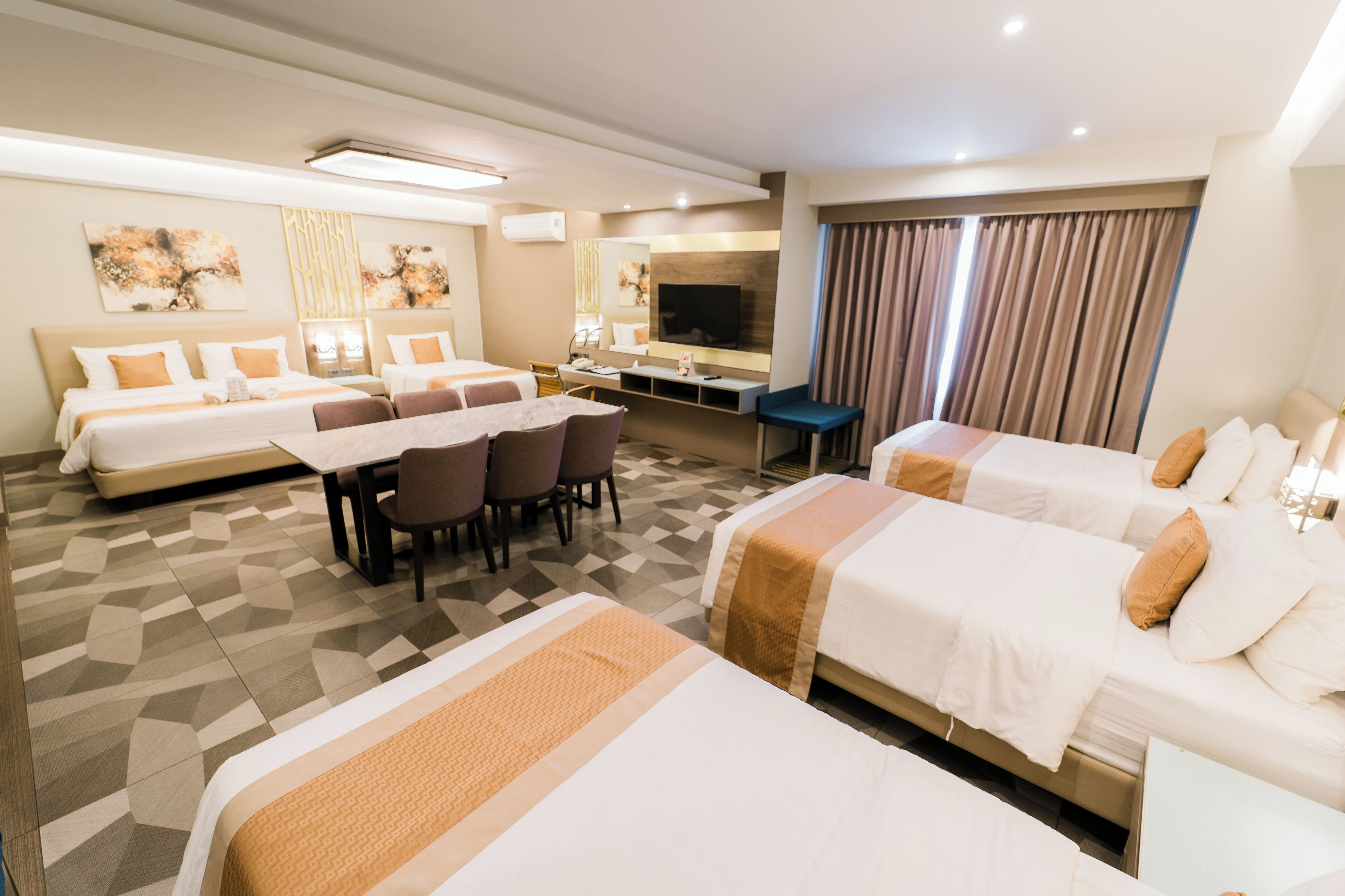 A hotel room with two beds, a dining area, a TV, and a large window with curtains.