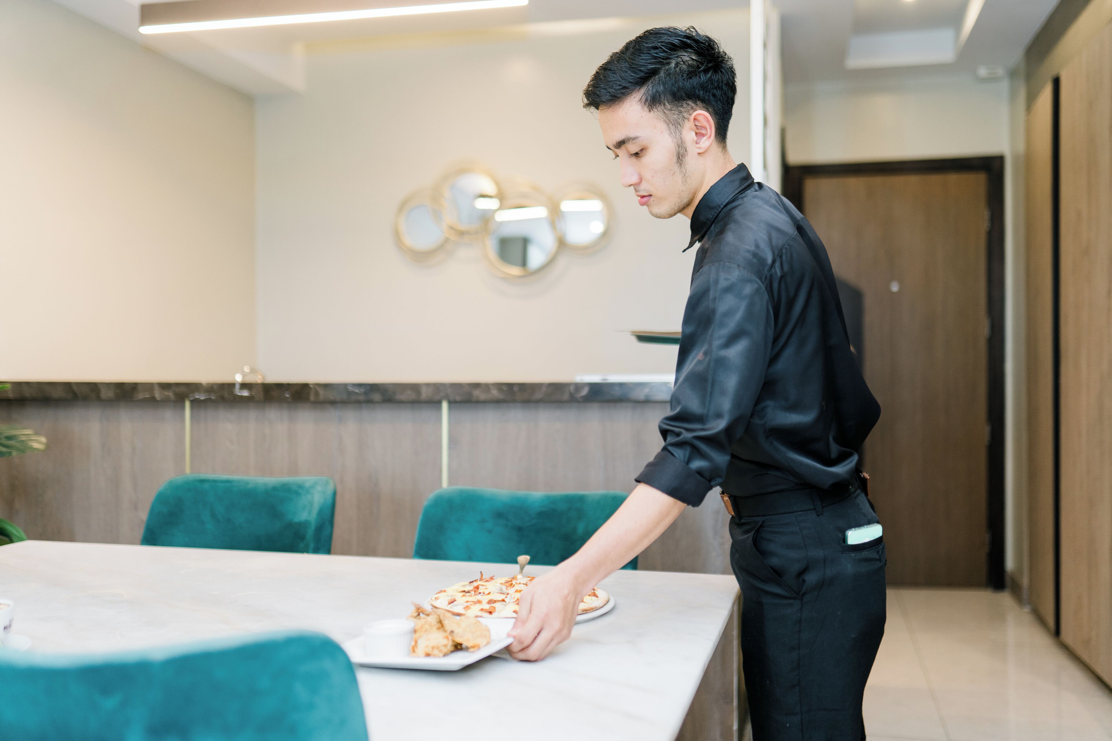 A person serving food at a table in a modern dining area with teal chairs and a marble table.