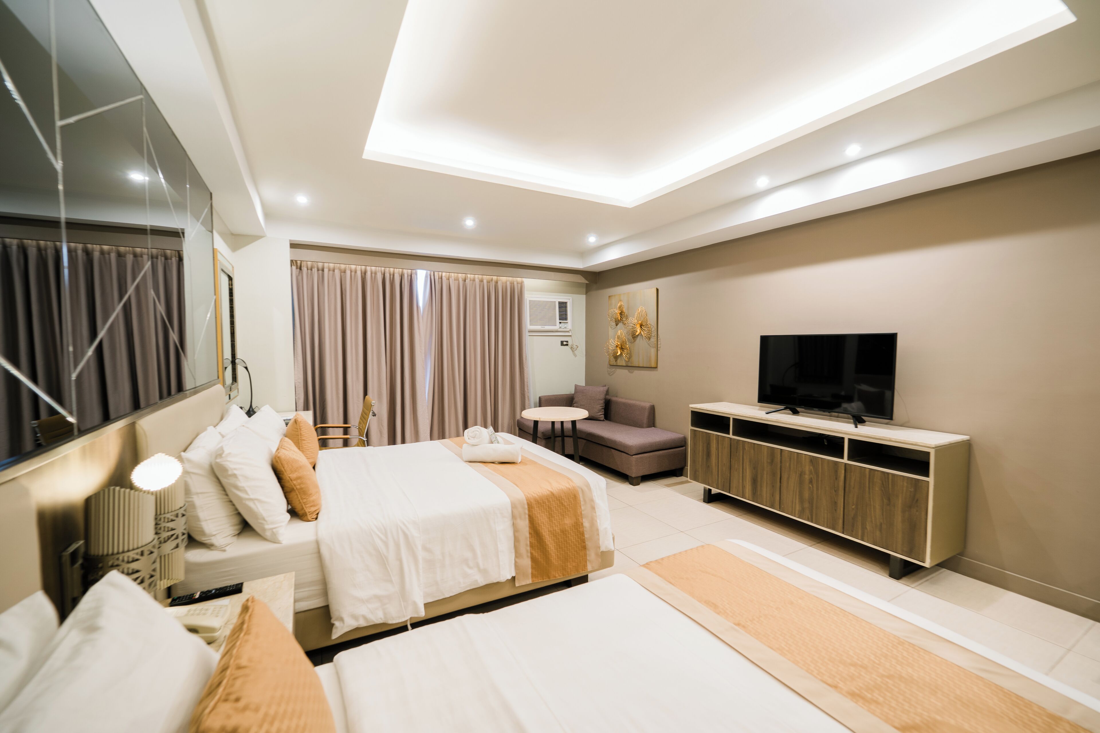 A modern hotel room with a large bed, a sofa, a TV, and a minibar.