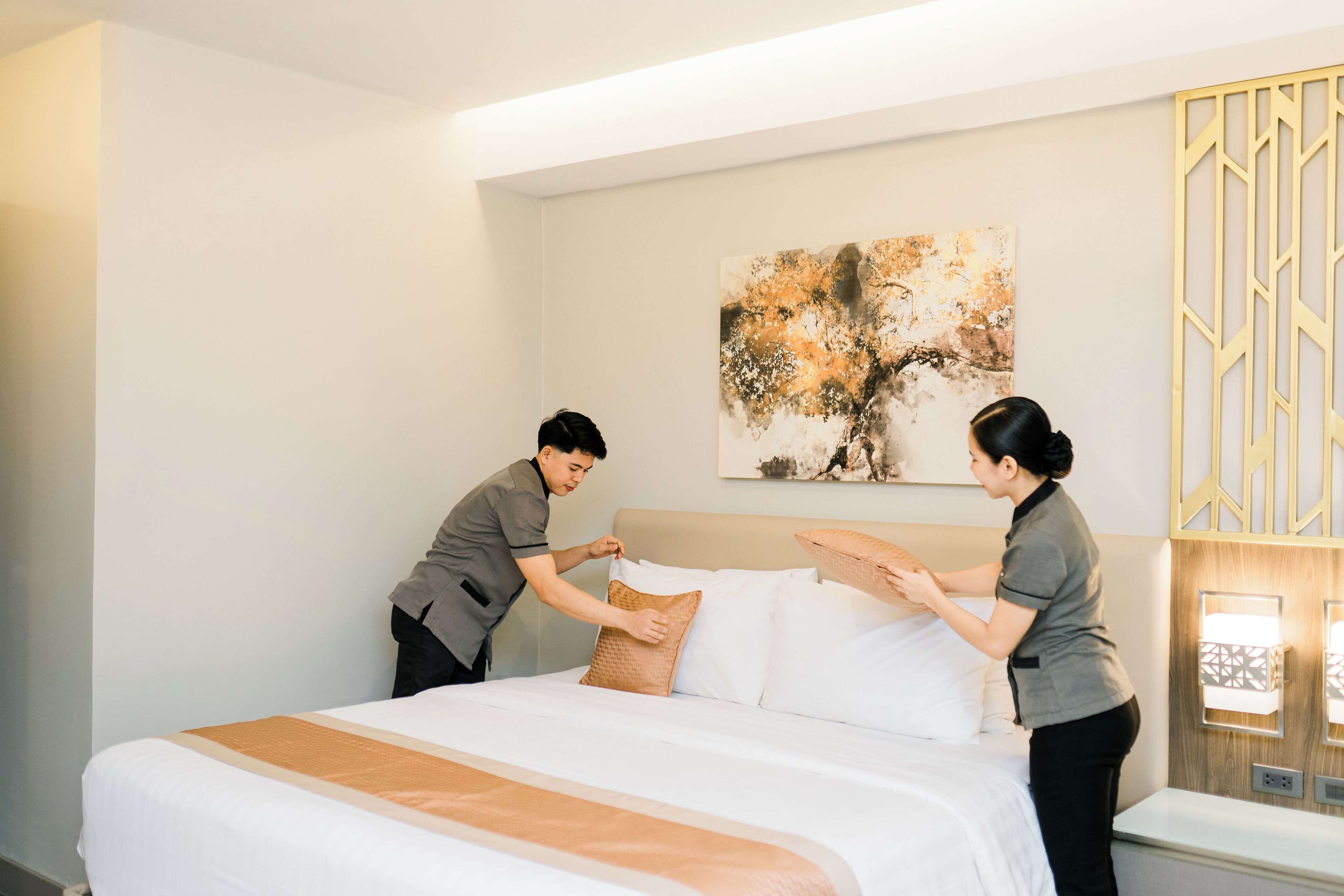 A hotel room with a neatly made bed, a large abstract painting on the wall, and a decorative wall panel.