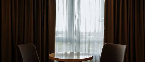 Une pièce avec deux chaises et une table ronde, des rideaux et une fenêtre avec des rideaux légers.