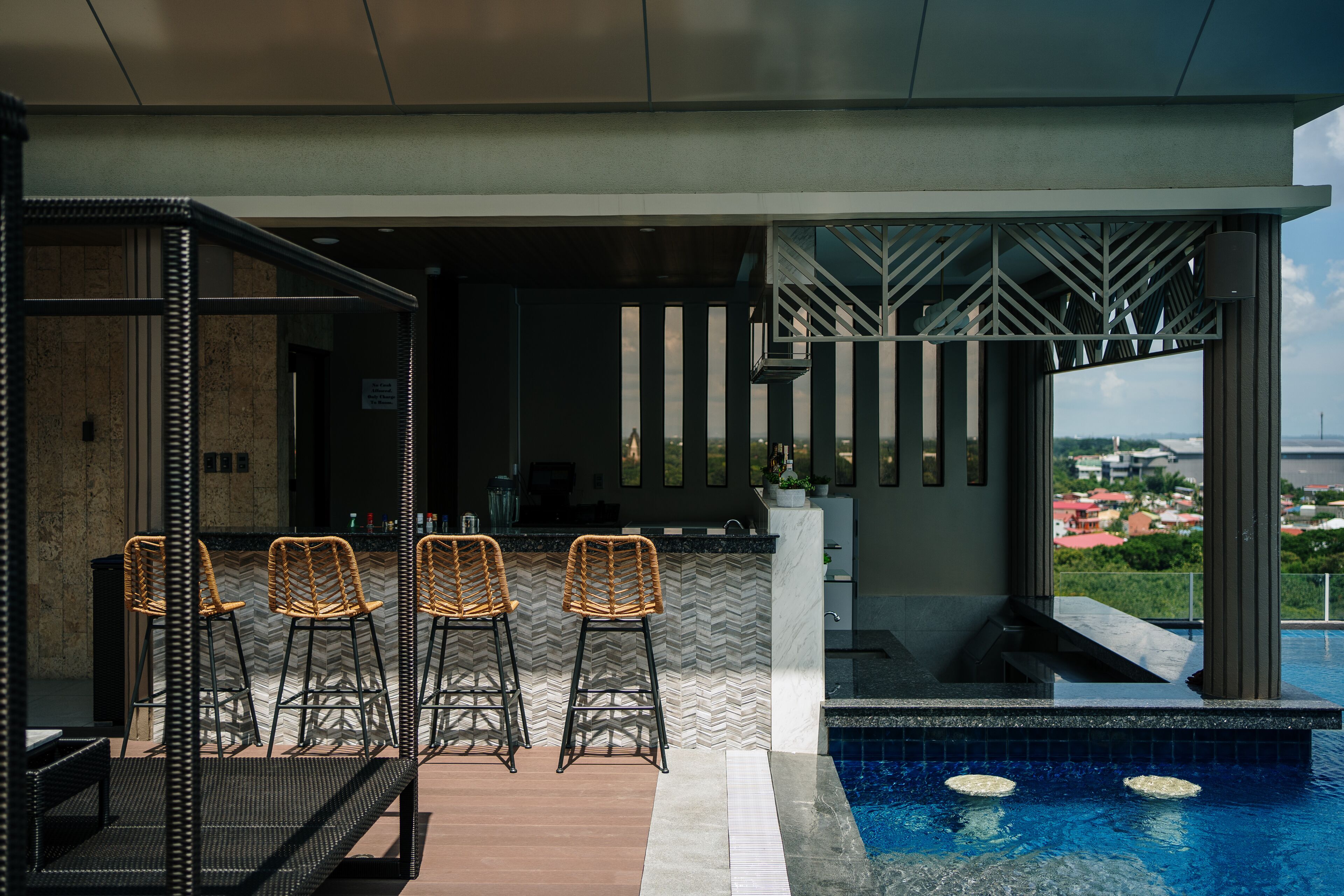Eine moderne Außenbar mit Korbstühlen, einem Pool und Blick auf die Stadt.