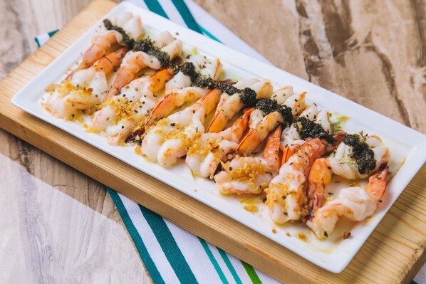 Une assiette rectangulaire blanche, sur laquelle on a disposé des crevettes cuites et des bouquets de brocoli, le tout présenté sur une planche en bois.