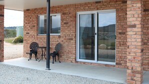 Un bâtiment en briques doté d’un patio couvert comprenant deux chaises en métal et une table.