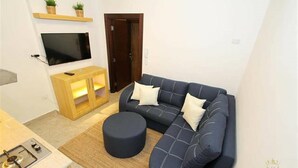 Sala de estar con sofá, reposapiés, televisor y mueble de madera.