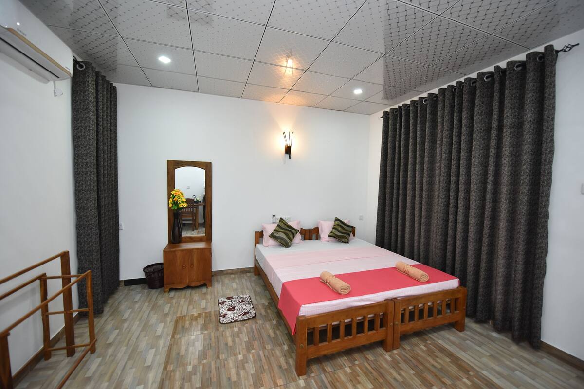 A bedroom with a wooden bed, a bedside table, a mirror, and a small stool.