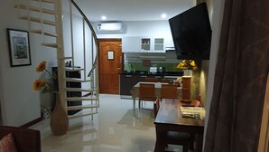 A spacious living area with a staircase, a dining table, and a kitchen in the background.