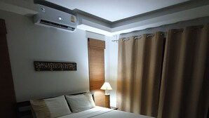 A hotel room with a bed, a bedside lamp, an air conditioning unit, a window with curtains, and a wall-mounted sign.