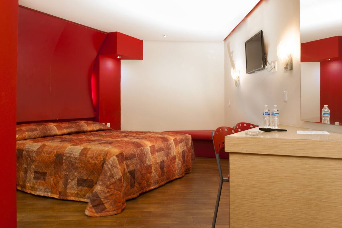 A hotel room with a bed, a desk, a chair, a TV, and a mirror.