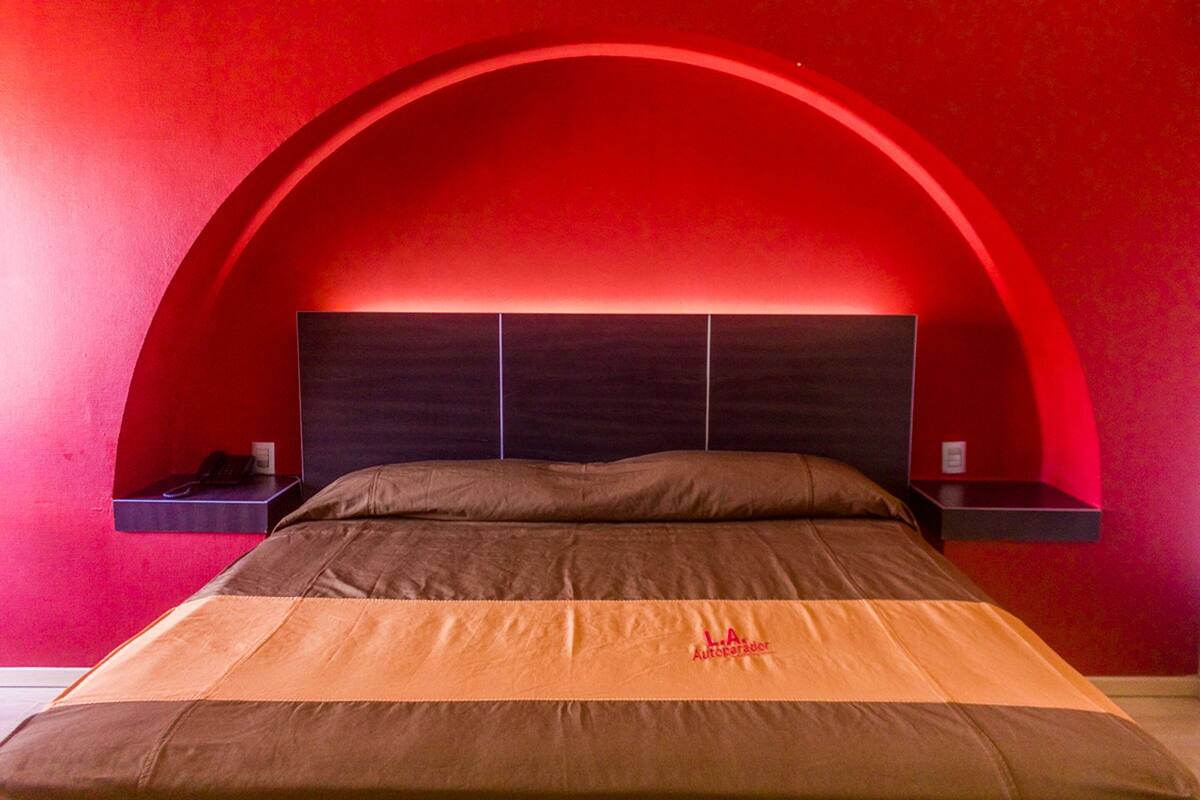 A bed with a brown and orange bedspread, a dark headboard, and a red arched ceiling.