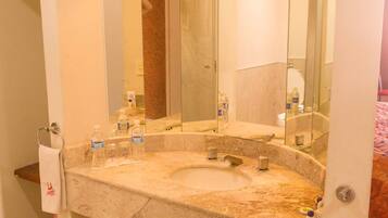 Un baño con lavabo de mármol, dos grifos, un perchero para toallas y un espejo.