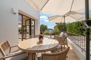 A round wooden table with chairs, a potted plant, and a white umbrella on a balcony. - Modern and  luxury villa in Moraira, Costa Blanca, Spain  with heated pool for 6 persons (Moraira)