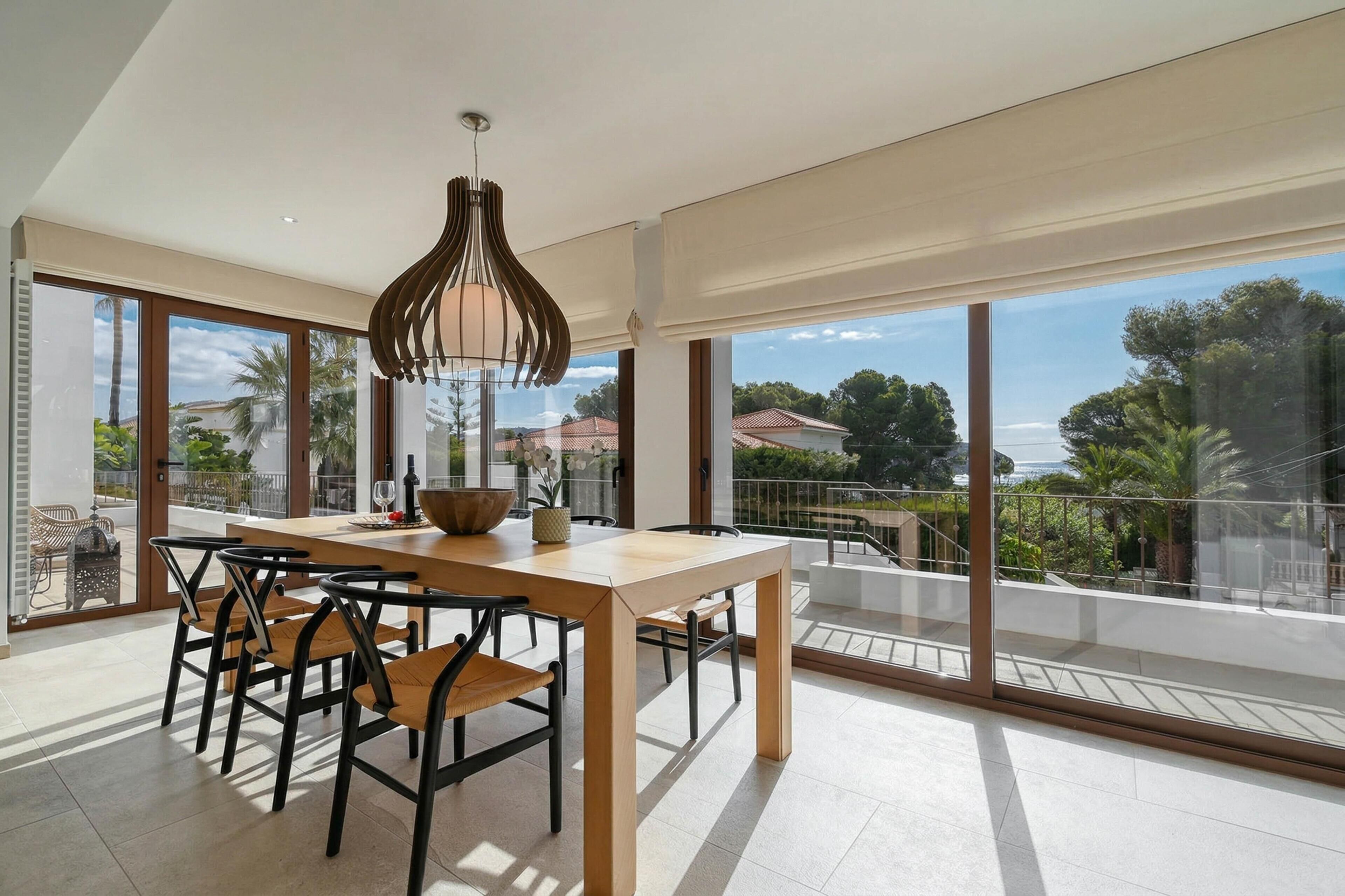 Un comedor moderno con una mesa y sillas de madera, una lámpara colgante y grandes ventanales que ofrecen vistas al exterior.