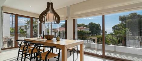 Un comedor moderno con una mesa y sillas de madera, una lámpara colgante y grandes ventanales que ofrecen vistas al exterior.