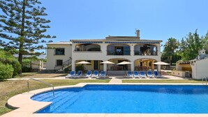 A two-story house with a swimming pool, lounge chairs, and umbrellas.