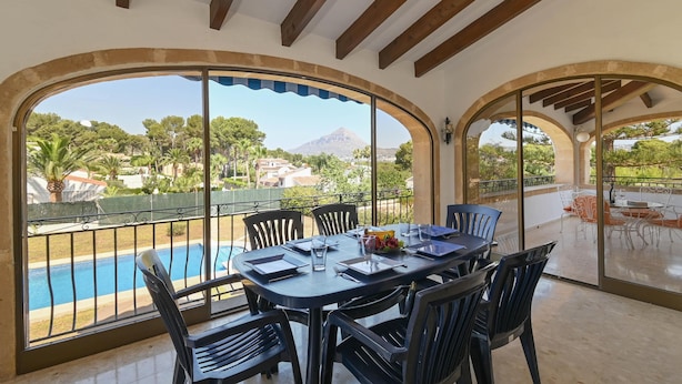 A dining area with a view of a swimming pool and a mountain in the background.