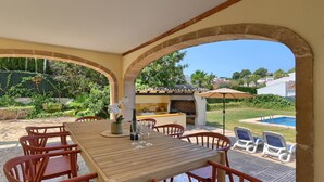 An outdoor patio with a wooden table and chairs, a barbecue area, and a pool in the background. - Jasmin 10 pax - Javea, Costa Blanca (Javea)