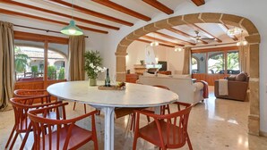 A spacious dining area with a round table and red chairs, an open kitchen, and a cozy living area with a sofa and a chair. - Jasmin 10 pax - Javea, Costa Blanca (Javea)
