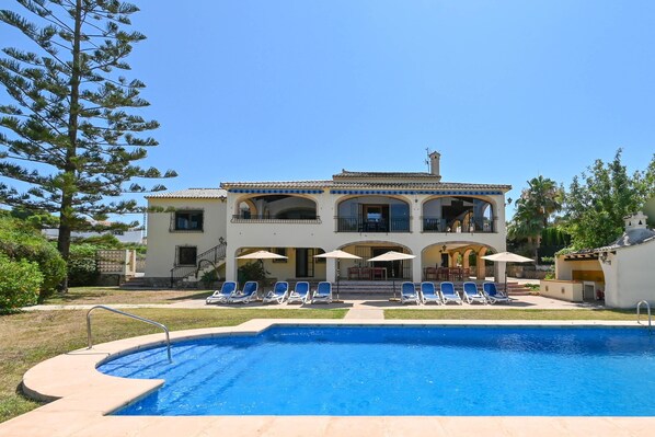 A two-story house with a swimming pool, lounge chairs, and umbrellas.