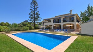 A large swimming pool with lounge chairs and umbrellas, surrounded by a well-maintained lawn and a multi-story building with balconies. - Jasmin 6 pax - Javea, Costa Blanca (Javea)