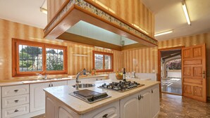 A spacious kitchen with white cabinetry, a central island with a stove, and large windows offering views of the outdoors. - Jasmin 6 pax - Javea, Costa Blanca (Javea)