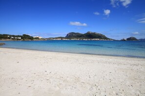 A beach with clear blue water, a sandy shore, and a mountain in the background.