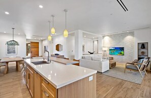 Relax in this open-plan living space with a kitchen island, dining table, and comfortable seating area featuring a sofa and armchairs.