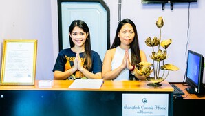 A reception desk with a framed certificate, a sign reading "Bangkok Canalé Home @Khaosan," and a decorative flower arrangement. - Bangkok Canale Home (Bangkok)