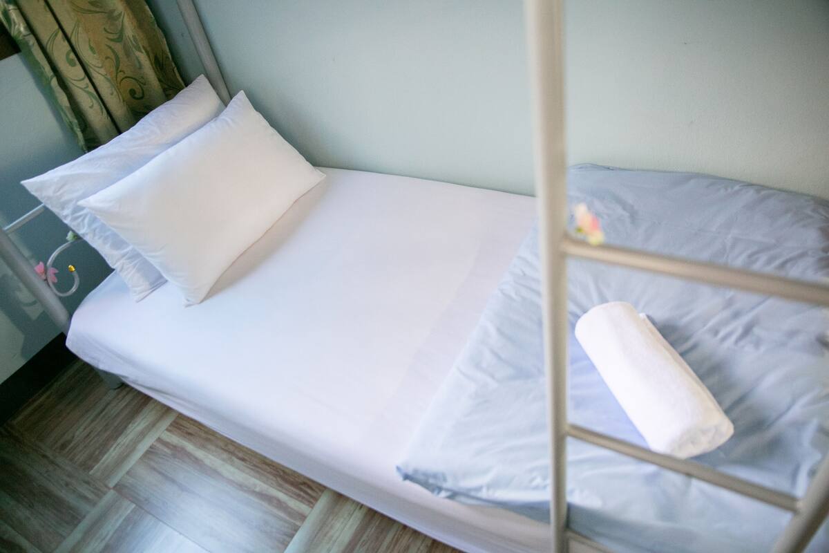 A single bed with white bedding and a rolled towel on the side.