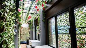 A cozy indoor space with a wooden bench, tables, and a view through a window with a metal grid. - Bangkok Canale Home (Bangkok)
