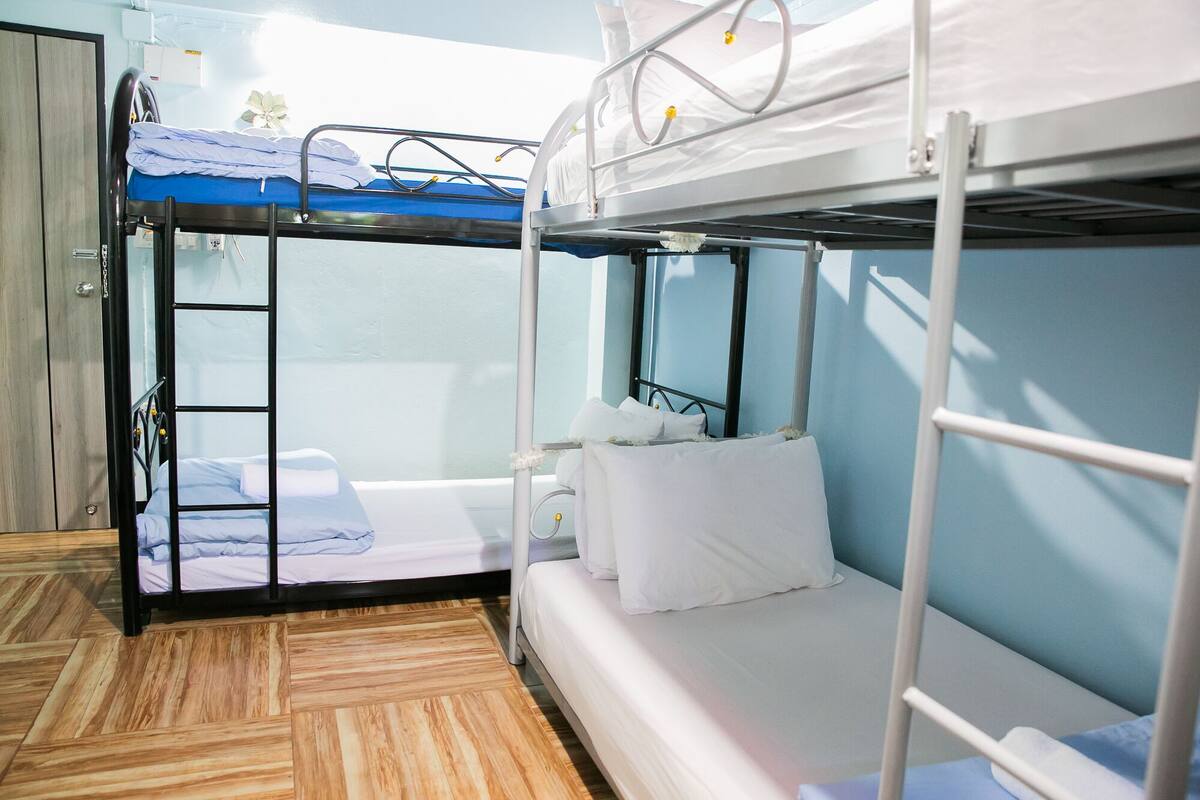 A bunk bed room with a wooden floor, a window, and a door.