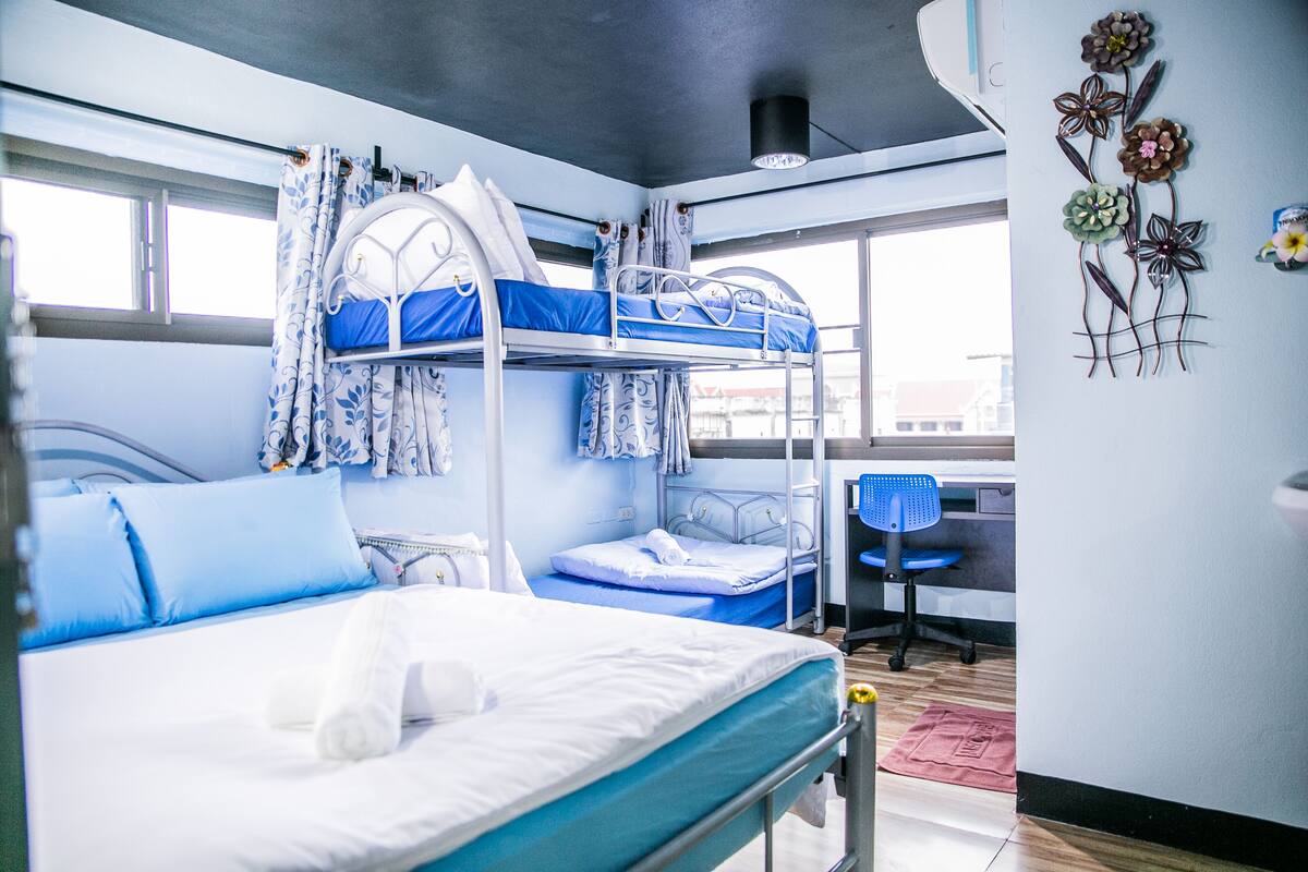 A bunk bed room with a desk and chair, a window, and a decorative wall piece.