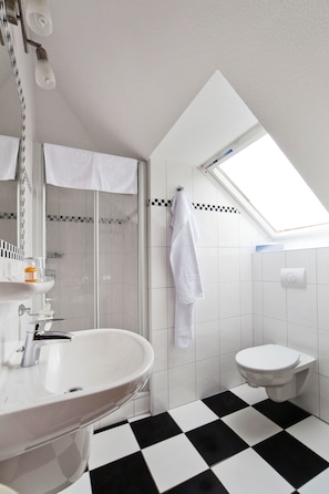 A modern bathroom with a black and white checkered floor, a skylight, a white sink, and a toilet.