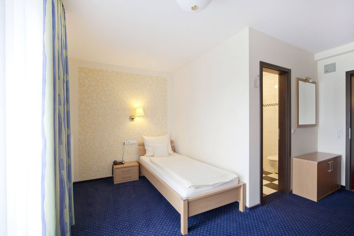 A hotel room with a bed, bedside table, lamp, and a mirror on the wall.
