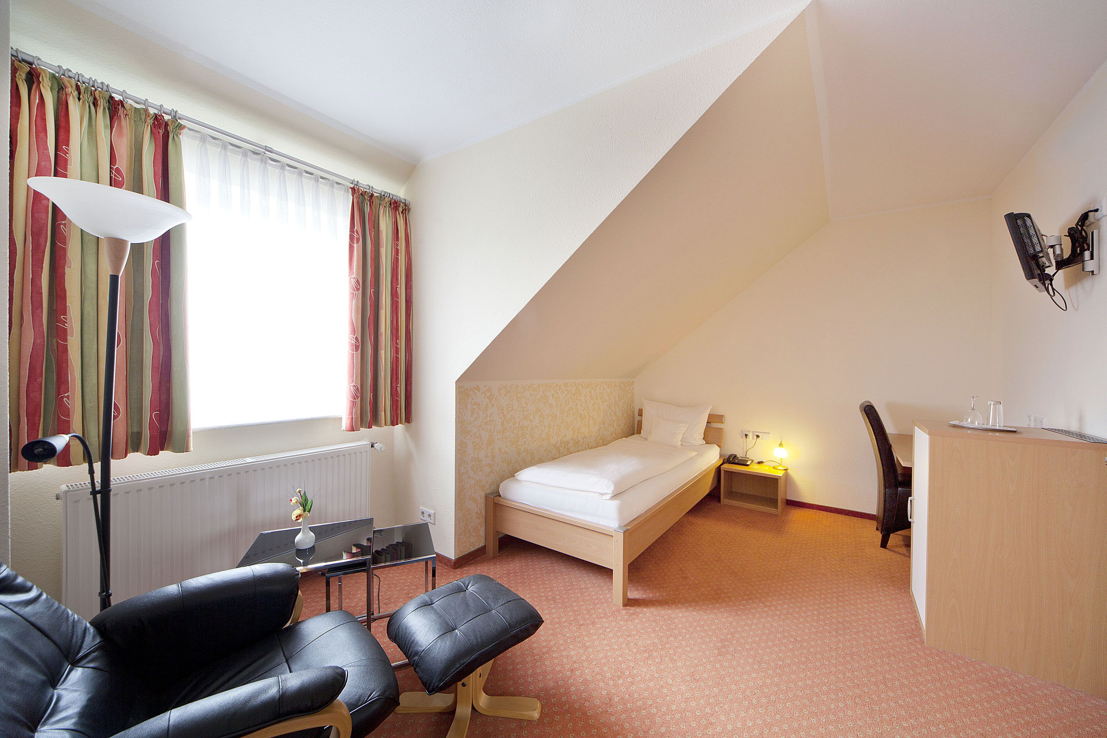 A bedroom with a single bed, a desk, a chair, and a lamp.