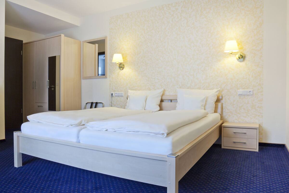 A hotel room with a double bed, a nightstand, a mirror, and two wall-mounted lamps.