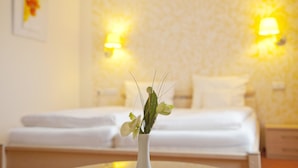 Habitación de hotel con una cama, un florero con flores y dos lámparas de pared.