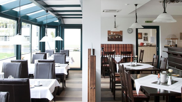 Un restaurante con un amplio salón comedor, mesas y sillas de madera. Hay luces colgantes y vistas al exterior.